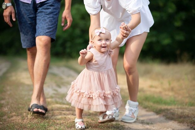 Una niña feliz de un año está siendo retenida por papá y mamá. Niño pequeño caminando con sus padres.