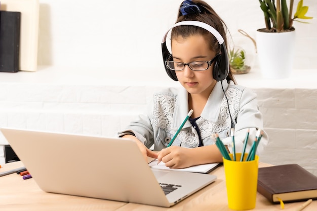 La niña feliz con auriculares con una computadora portátil sentada en la mesa en casa