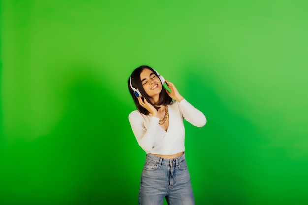 Niña feliz con auriculares escucha música y mantiene los ojos cerrados sobre una superficie verde en el estudio.