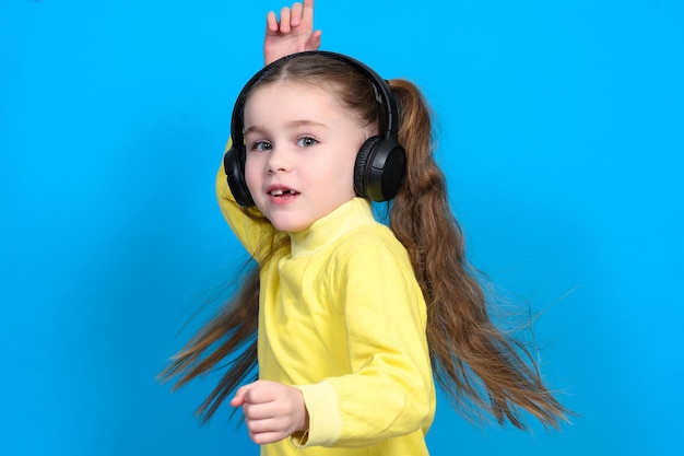 Niña feliz con auriculares inalámbricos sobre un fondo azul.