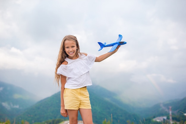 Niña feliz con avión de juguete en manos en las montañas