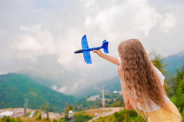 Niña feliz con avión de juguete en manos en las montañas