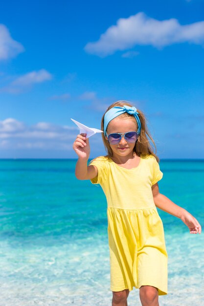 Niña feliz con avión de papel en manos en la playa de arena blanca