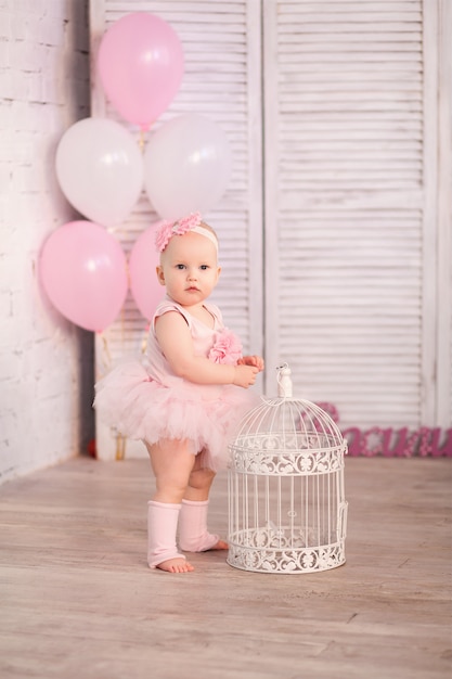 Foto niña feliz bailarina de 1 año en studio en pared de luz con bolas de color rosa