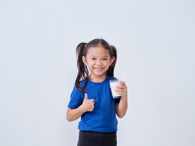 Niña feliz bebiendo leche y mostrando el pulgar hacia arriba signo contra la luz