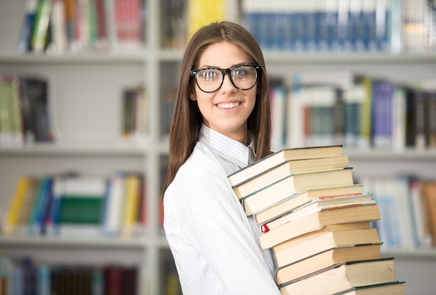 Niña feliz en la biblioteca de la Universidad sosteniendo la pila de libros