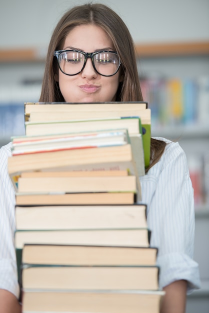 Niña feliz en la biblioteca de la Universidad sosteniendo la pila de libros