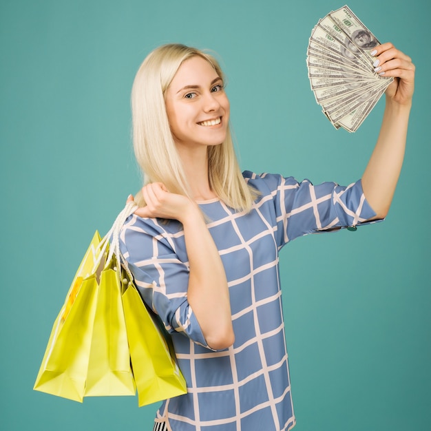 Niña feliz en una blusa a cuadros tiene billetes de cien dólares y bolsas de la compra.