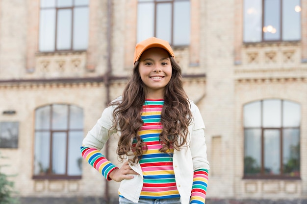 Niña feliz con cabello largo y rizado niño bonito sonriendo al aire libre niño belleza y moda colegiala alegre usar gorra adolescente en estilo casual concepto de peluquería felicidad infantil