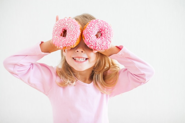 Niña feliz con cabello rubio jugando y probando donas con glaseado rosa en la celebración de hanukkah