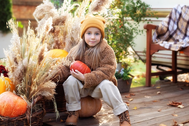 niña feliz con calabaza al aire libre en halloween y jugando cerca de casa en el jardín de otoño