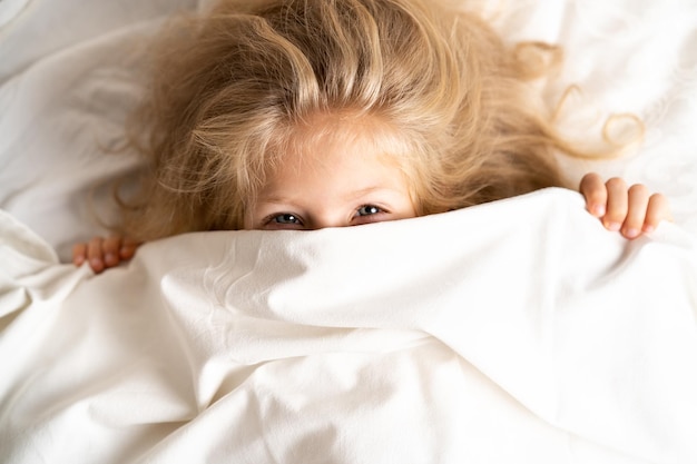 Niña feliz en una cama blanca sobre una almohada buenos días concepto de sueño saludable para bebés