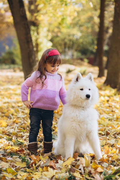 Niña feliz camina con un perro Samoyedo blanco en el parque otoño
