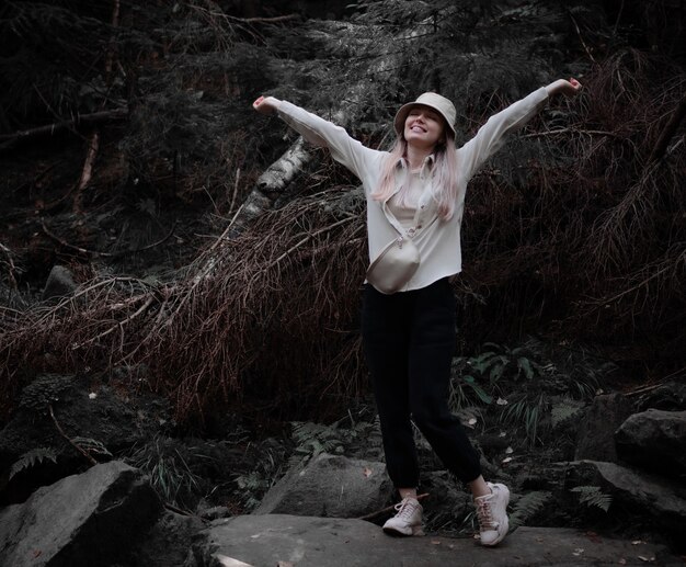 Niña feliz con una camisa beige y un sombrero se encuentra en una piedra en el bosque