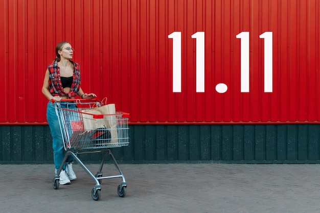 Niña feliz con carrito de compras sobre fondo de tienda de pared roja con número de día 11.11