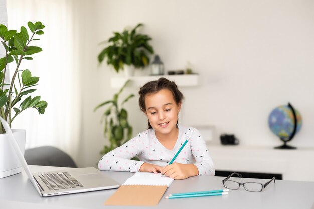 Niña feliz en casa trabajando con una computadora portátil