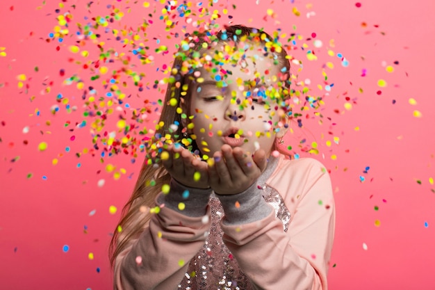 Foto niña feliz celebrando sopla confeti multicolor