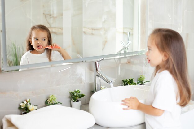 Foto una niña feliz se cepilla los dientes frente a un espejo en el baño. rutina de la mañana. higiene. foto de alta calidad