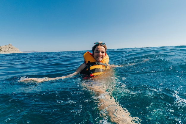 Niña feliz en un chaleco salvavidas nada en el agua del mar en el verano de vacaciones