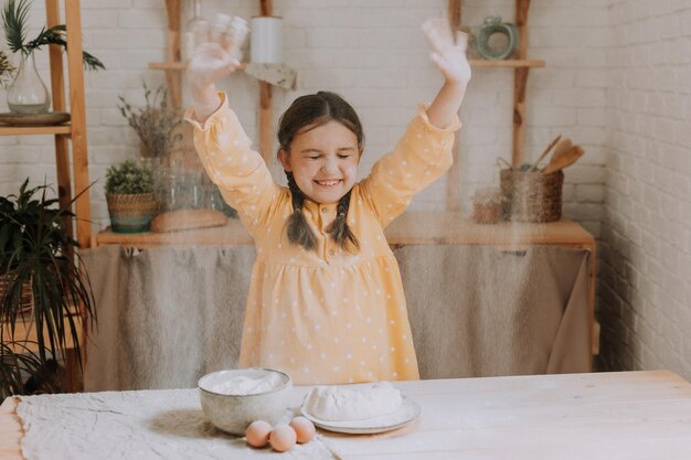 una niña feliz cocina un pastel en la cocina con un vestido de algodón