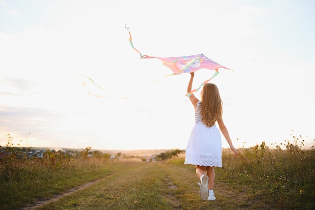 Foto niña feliz con una cometa corriendo en la pradera en verano en la naturaleza