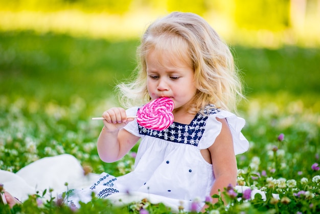 Niña feliz comiendo un caramelo en un palo en forma de corazón. Concepto de San Valentín