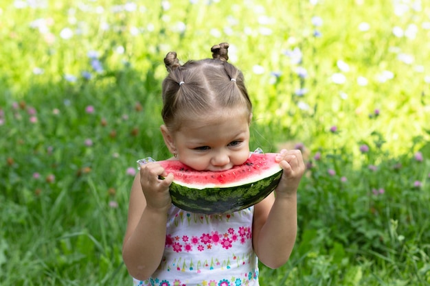 Niña feliz comiendo melón de agua en el parque de verano