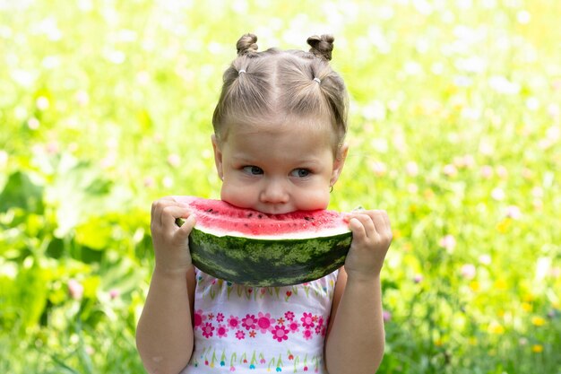 Niña feliz comiendo melón de agua en el parque de verano