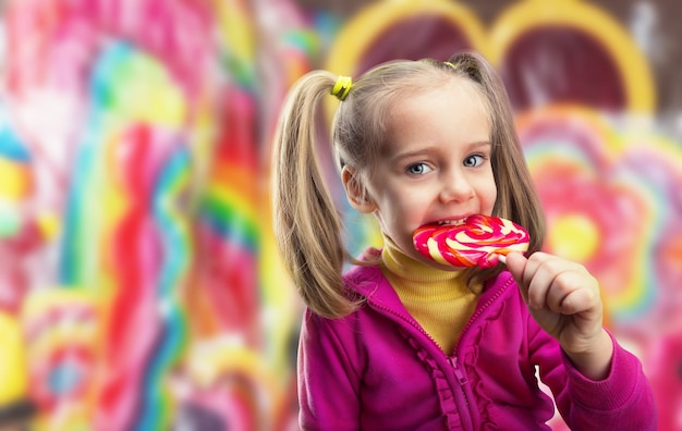 Niña feliz comiendo piruletas sobre superficie multicolor