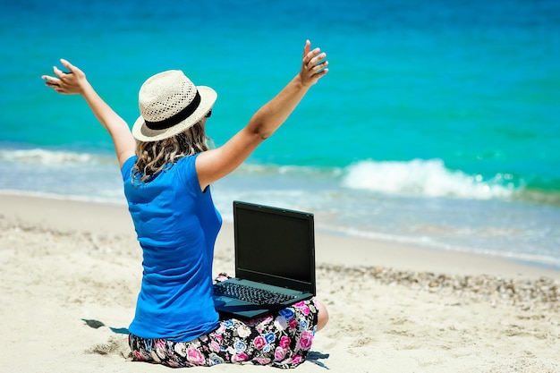 Una niña feliz con una computadora portátil cerca del viaje de fin de semana junto al mar