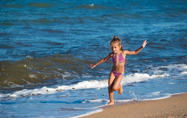 Niña feliz corre a lo largo de la orilla arenosa