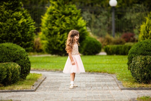 Foto niña feliz corriendo por el callejón de árboles y arbustos hermosos decorados
