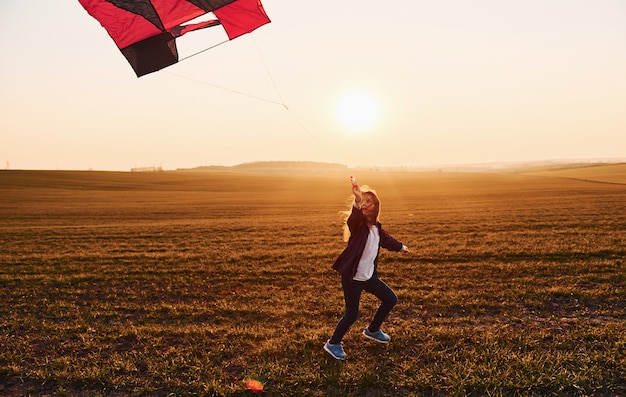 Niña feliz corriendo con la cometa en las manos en el hermoso campo al amanecer