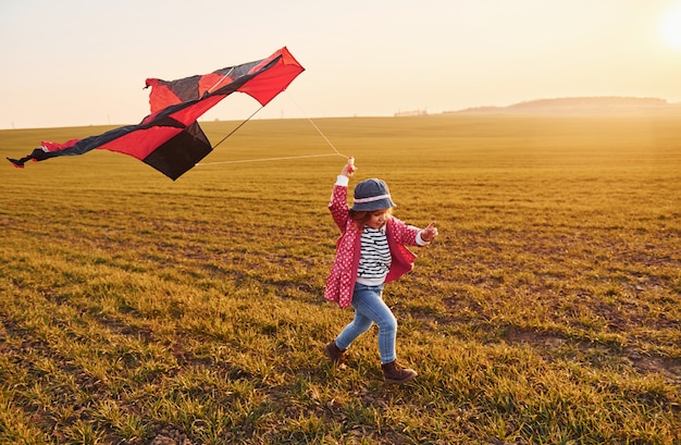 Niña feliz corriendo con la cometa en las manos en el hermoso campo al amanecer