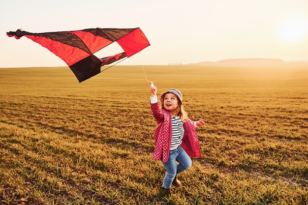 Niña feliz corriendo con la cometa en las manos en el hermoso campo al amanecer