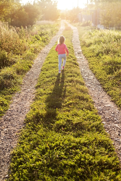 Niña feliz corriendo por las pistas de campo en el prado en un día soleado