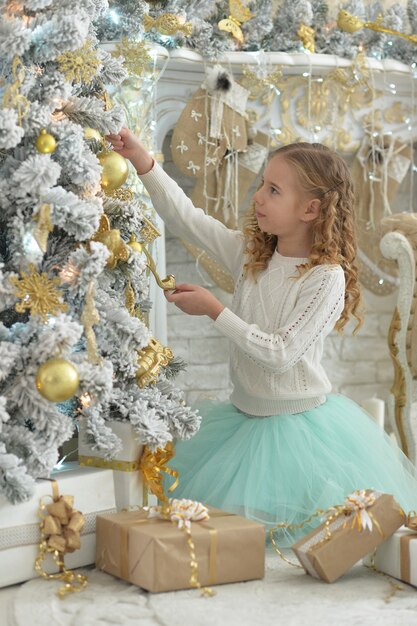 Niña feliz decorando el árbol de Navidad en casa