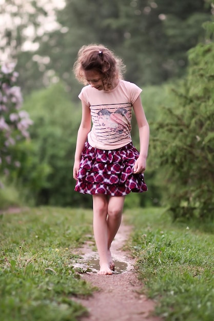 Niña feliz descalza camina a través de charcos de agua después de la lluvia de verano en el campo.