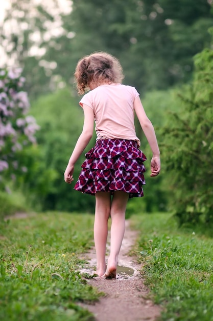 Niña feliz descalza camina a través de charcos de agua después de la lluvia de verano en el campo.