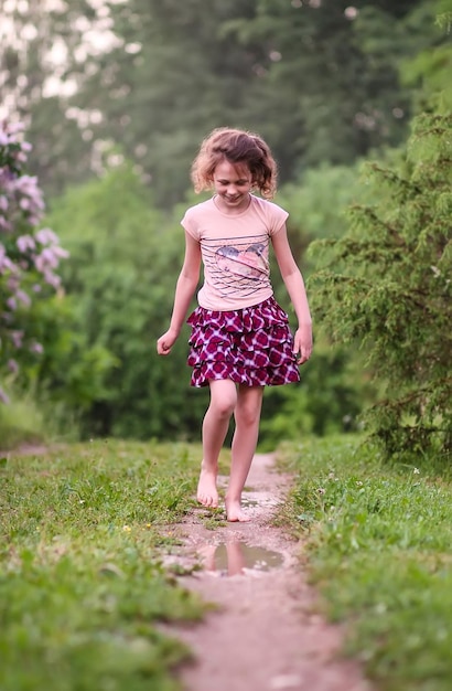 Niña feliz descalza camina a través de charcos de agua después de la lluvia de verano en el campo.