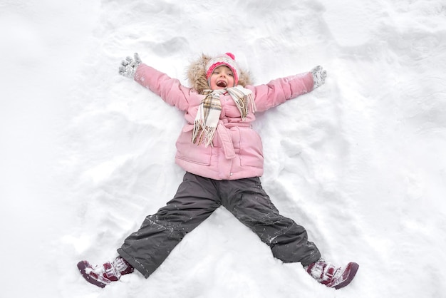 Una niña feliz desdentada en el paseo invernal en la naturaleza Un niño haciendo un ángel en la nieve