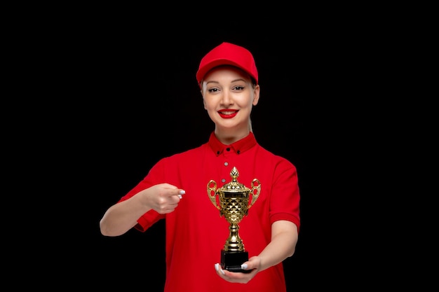 Niña feliz del día de la camisa roja señalando el precio con una gorra roja con camisa y lápiz labial brillante