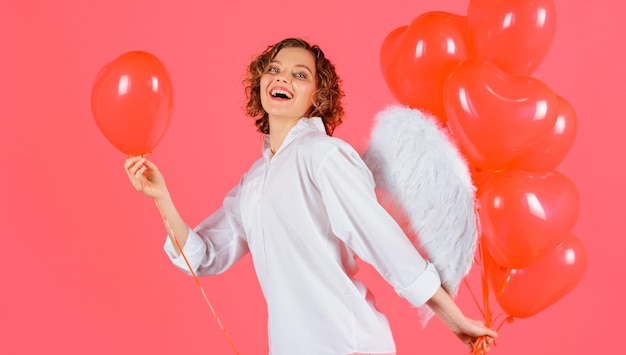 Niña feliz del día de san valentín con alas de ángel sostiene globos rojos en forma de corazón concepto de historia de amor
