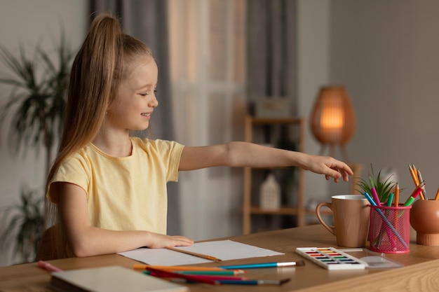 Niña feliz dibujando con lápices y pinceles en casa