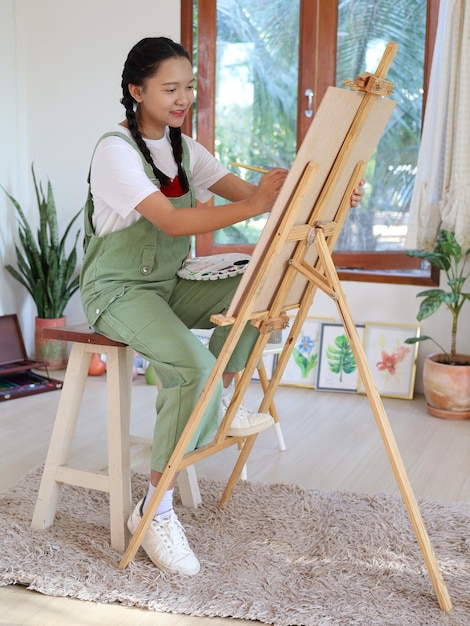 Niña feliz dibujando con una paleta de pintura y un pincel en casa, artista de pintura