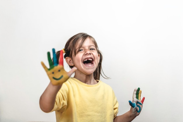 Niña feliz sin dientes con las manos pintadas riendo y divirtiéndose Niña que se pinta las manos con caras sonrientes y números Colores infantiles y concepto de felicidad Copiar espacio para texto