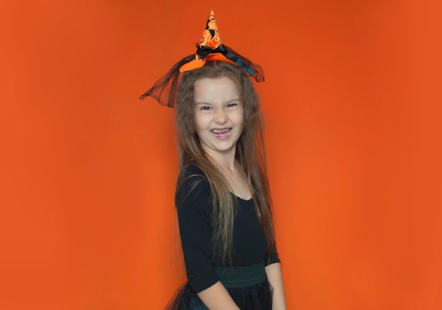 Niña feliz con un disfraz de bruja divirtiéndose en una celebración de Halloween en un fondo naranja aislado Listo para las vacaciones