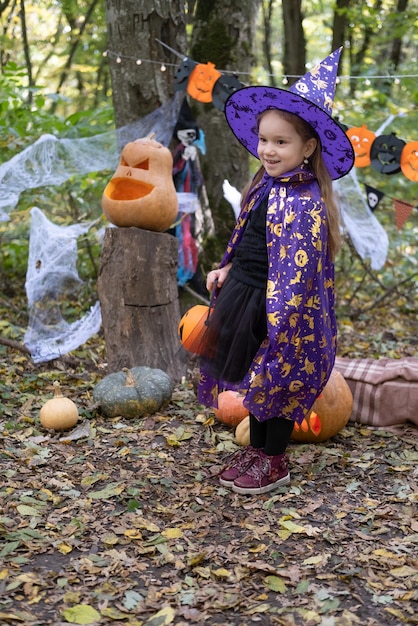 niña feliz en disfraz de halloween y sombrero de bruja con escoba en decoración de halloween al aire libre