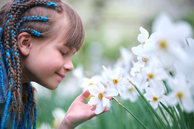 Niña feliz disfrutando del dulce olor de las flores de narciso blanco en el jardín de verano