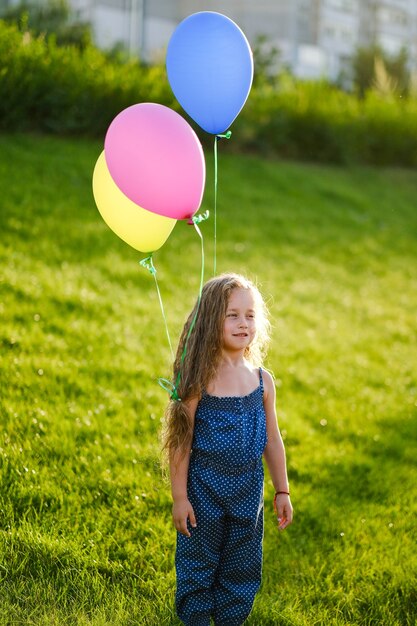 Niña feliz divirtiéndose y jugando con su hermoso cabello y globos en el parque en primavera. Infancia feliz.